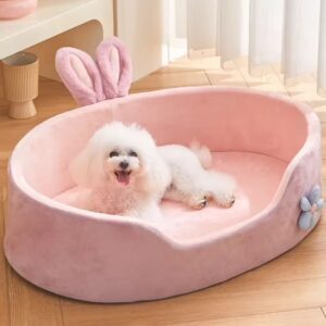Small white dog resting in a pink plush pet bed with bunny ears.