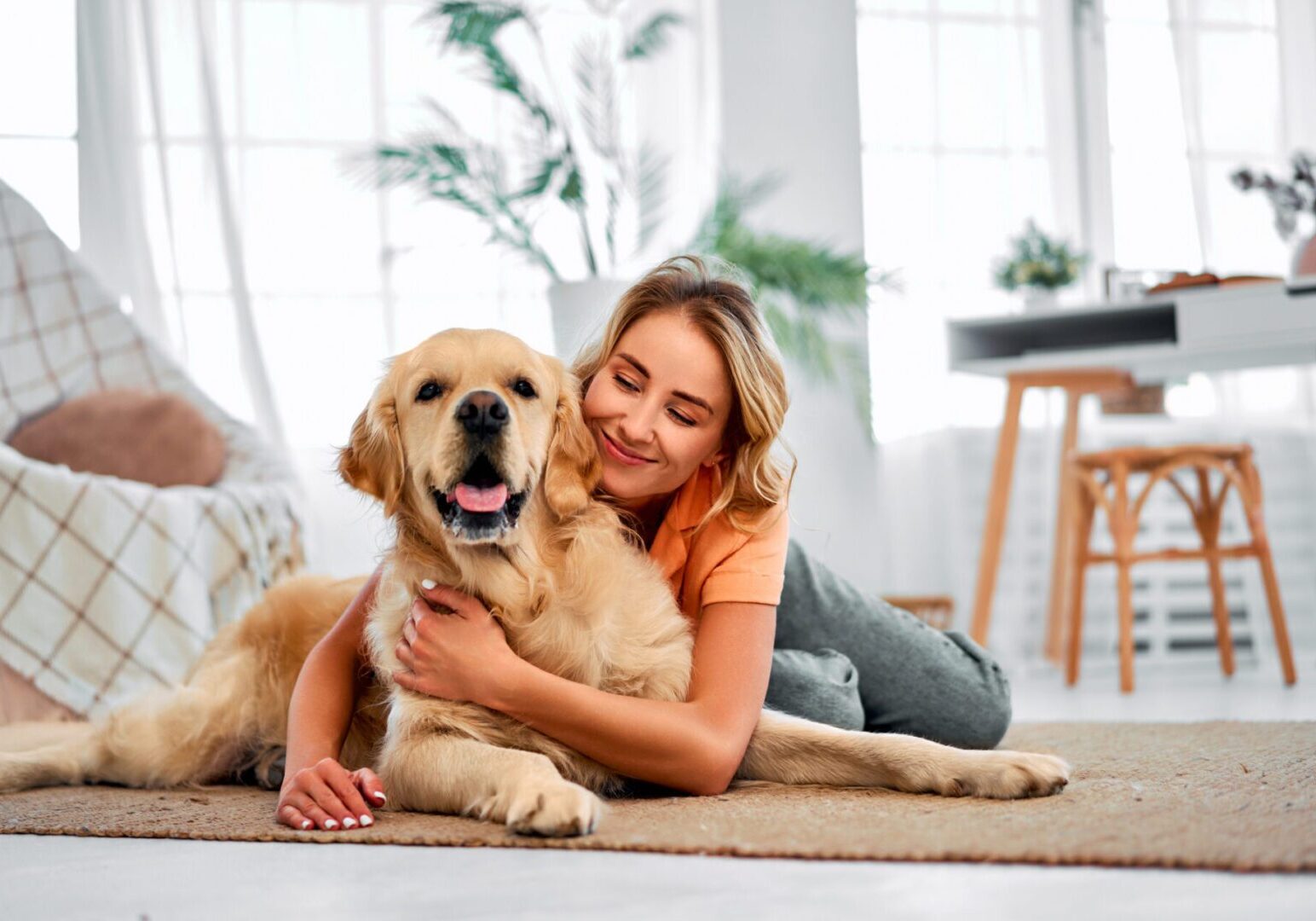 Woman happily hugging her golden retriever indoors.
